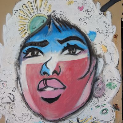 Expressive painted face with bold colors and whimsical details on an outdoor wall