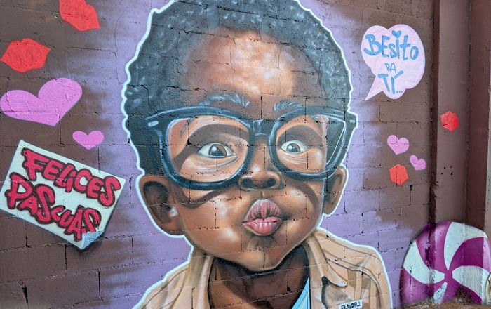 Hyperrealistic portrait mural of a child with glasses blowing a kiss